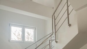 Una escalera moderna con barandales de metal, un ventanal con luz natural y un suelo de baldosas.