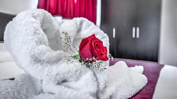 A bed with a white fluffy blanket and a red rose.