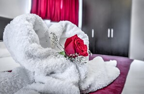 Een bed met een witte, pluizige deken en een rode roos.