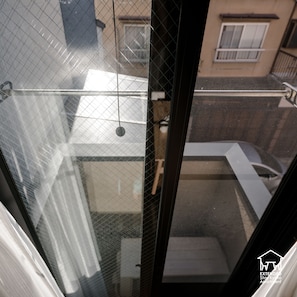 A view through a window with a metal grid, a balcony, and a building in the background. - EXTENDED Stay Kyoto Apartment (Kyoto)