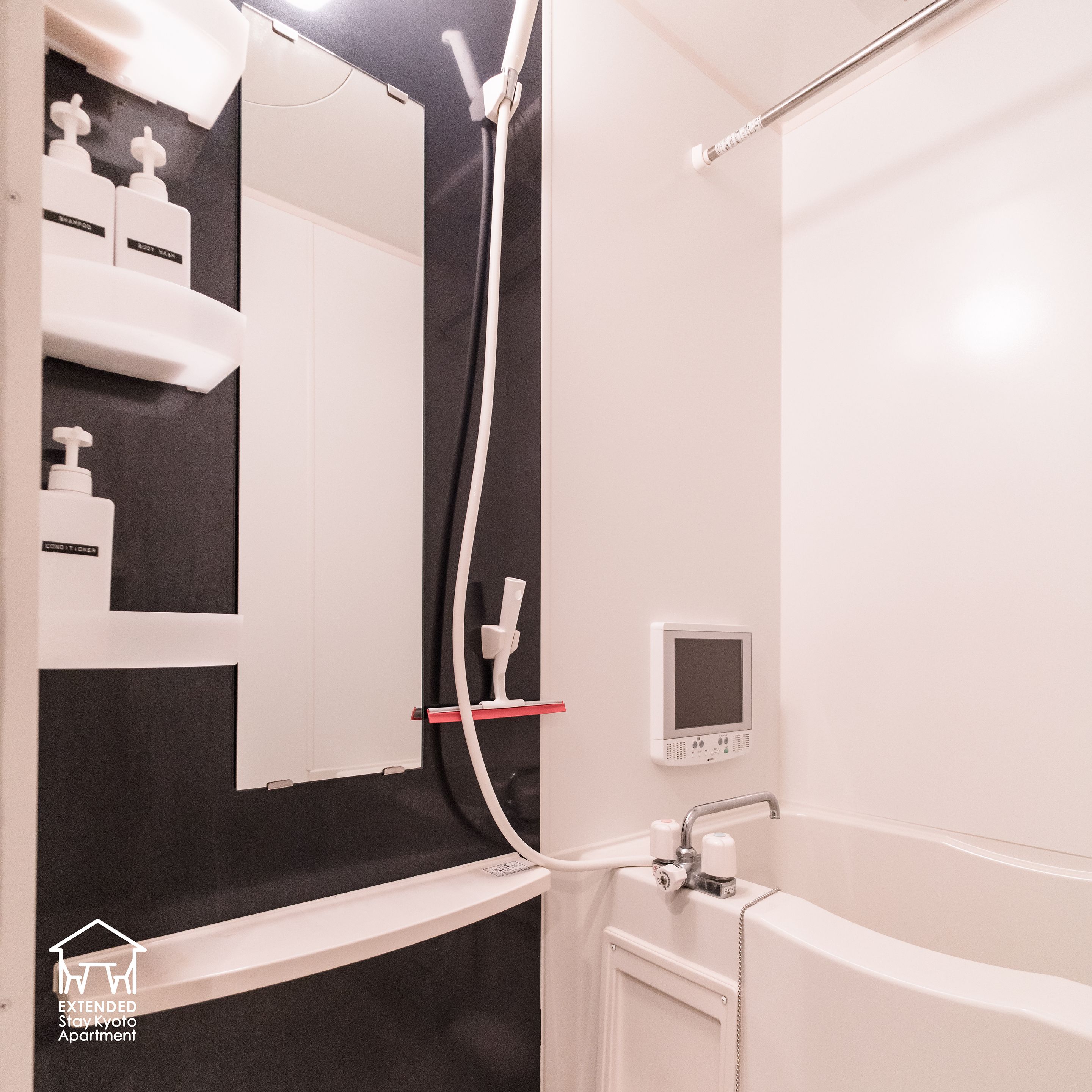 A modern bathroom with a shower, a toilet, and a sink. There is a mirror above the sink and a small screen on the wall.