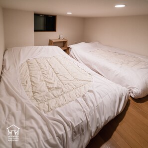 Two beds with white bedding in a room with wooden flooring and a small wooden nightstand. - EXTENDED Stay Kyoto Apartment (Kyoto)