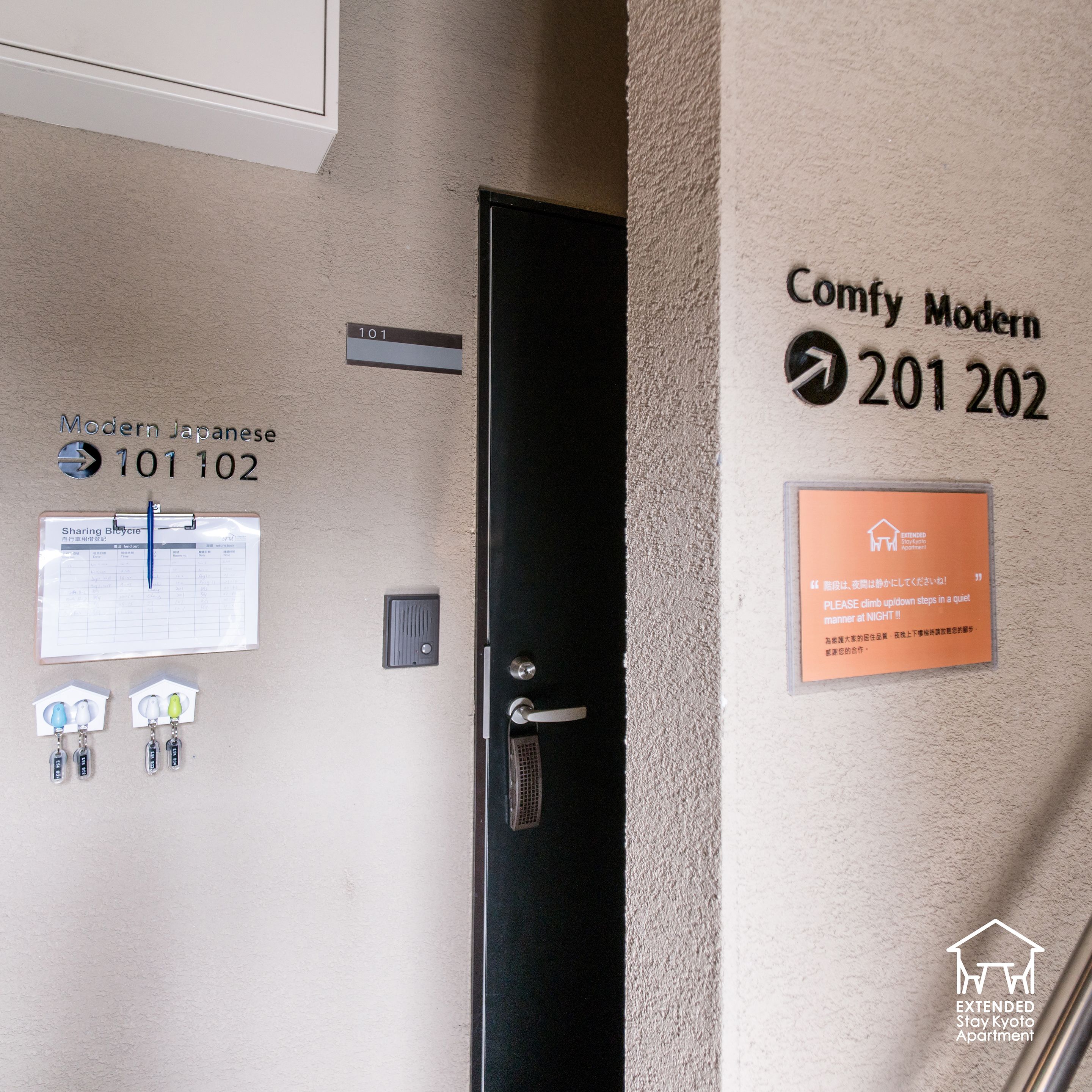 Hotellihuoneen sisäänkäynti, jossa on ovi, seinälle kiinnitetty kyltti, jossa lukee huone 201 ja 202, ilmoitustaulu, jossa on jaettu pyörä -merkki, ja avainkortin pidike avaimilla.