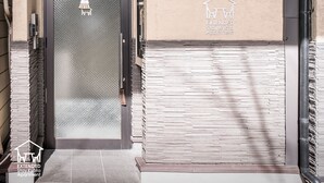 A building entrance with a textured door, a small wall-mounted light, and a logo for Extended Stay Kyoto Apartment. - EXTENDED Stay Kyoto Apartment (Kyoto)