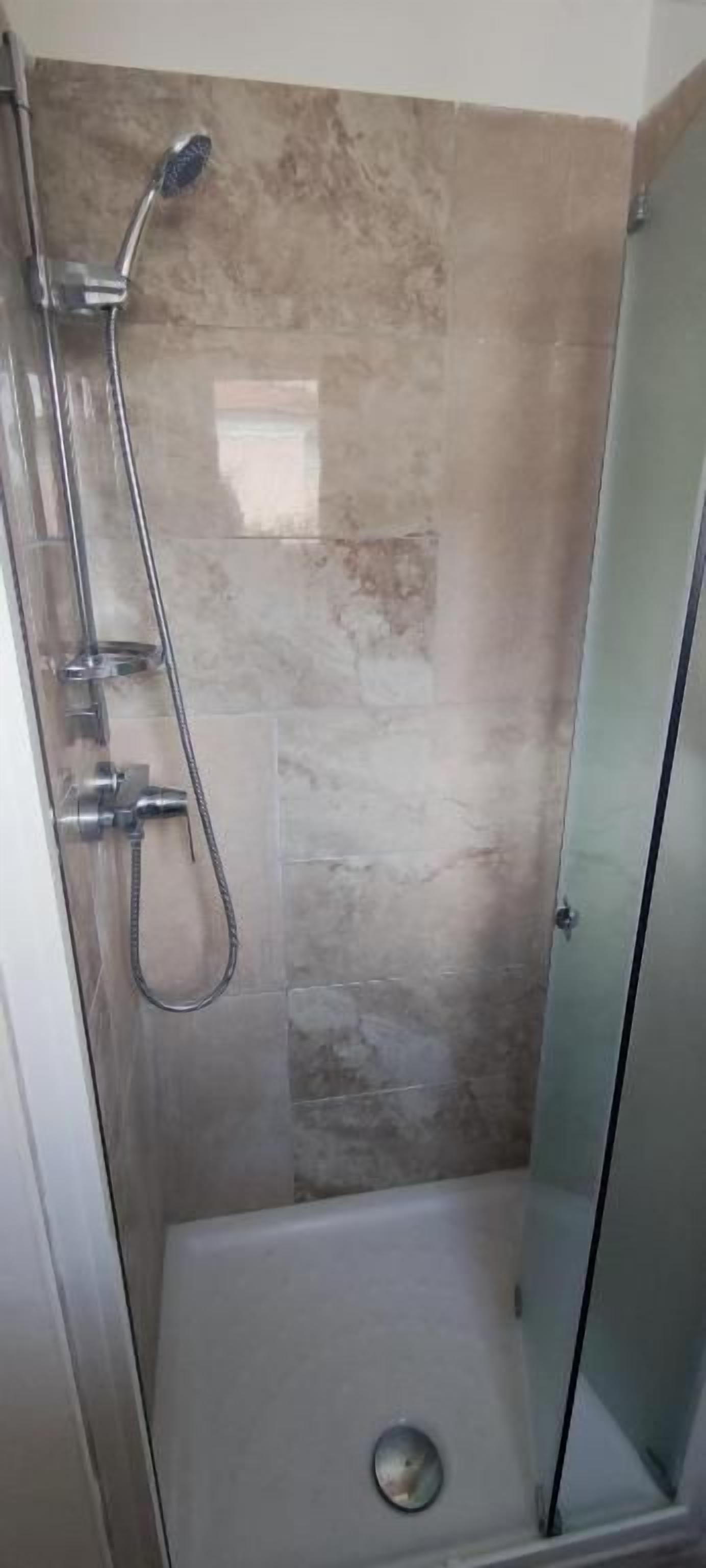 A shower with a glass door, a handheld showerhead, and a wall-mounted faucet.