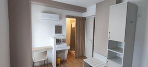 A small, clean room with a white sink, a mirror, a wardrobe, and a bench. - Vroom510 (Verona)