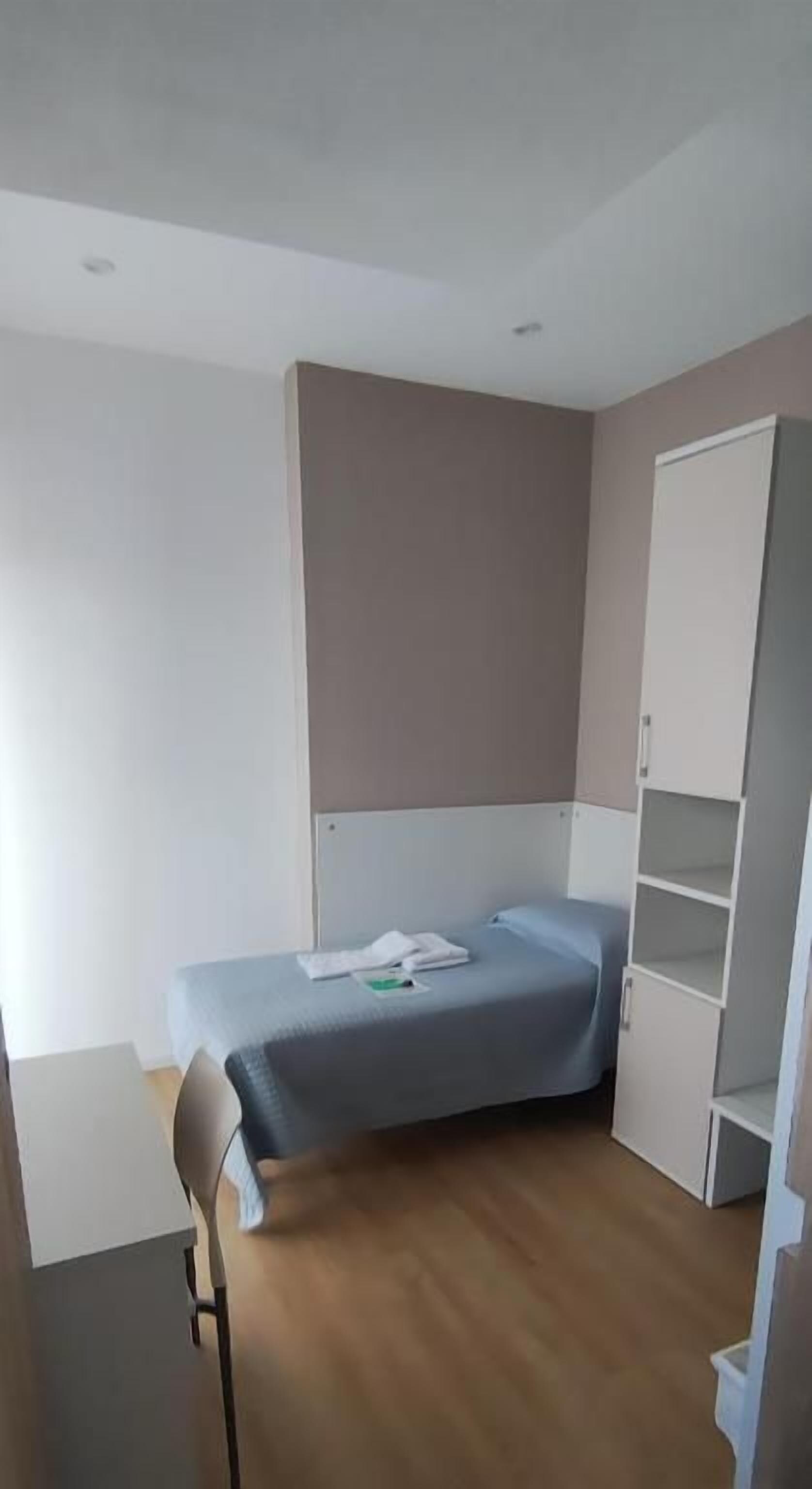 A room with a bed, a chair, a wardrobe, and a desk.