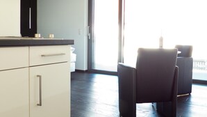 A modern kitchen with white cabinets and a black countertop, a dining area with two black chairs, and a large sliding glass door leading to a balcony. - Porta Vinea (Ruppertsberg)
