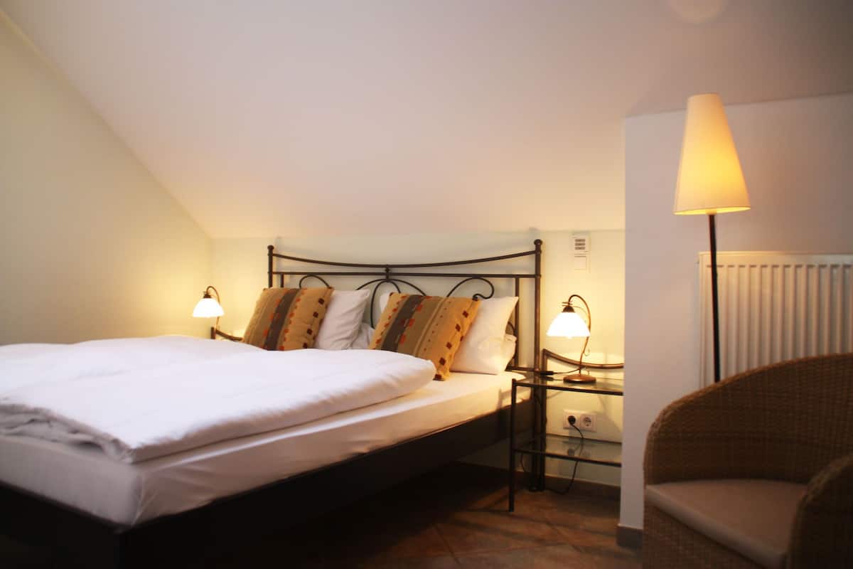 A bedroom with a bed, two bedside lamps, a chair, and a radiator.