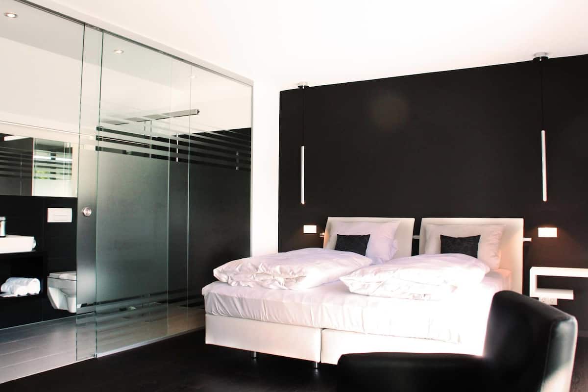 A modern bedroom with a glass partition, a white bed, and a black wall.
