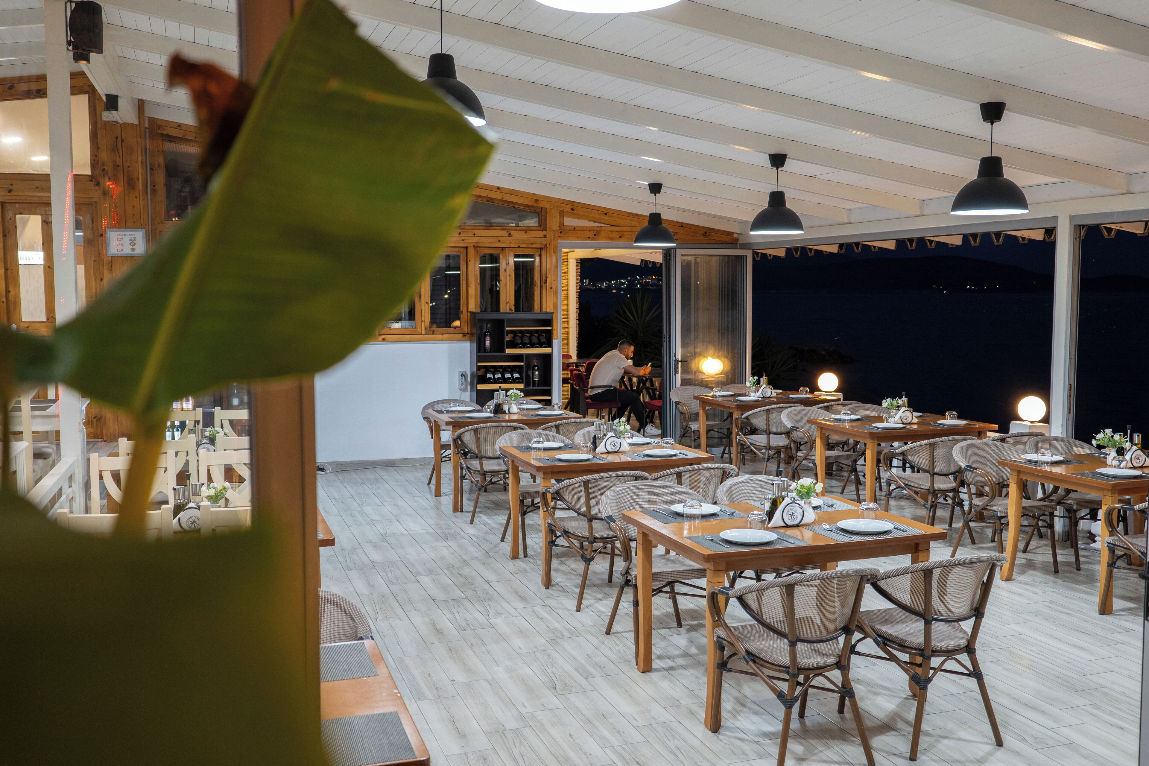 Un restaurante con mesas y sillas de madera, una zona de bar y amplios ventanales que ofrecen vistas del cielo nocturno.