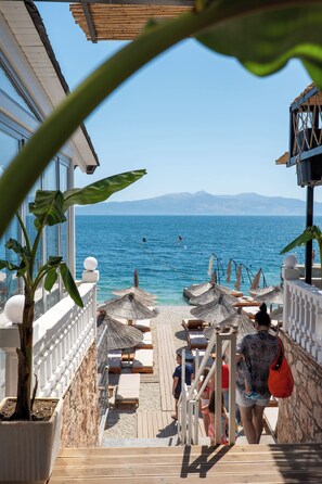 A deck with lounge chairs and umbrellas overlooking a beach. - Hotel Kompleks Joni (Sarandë)