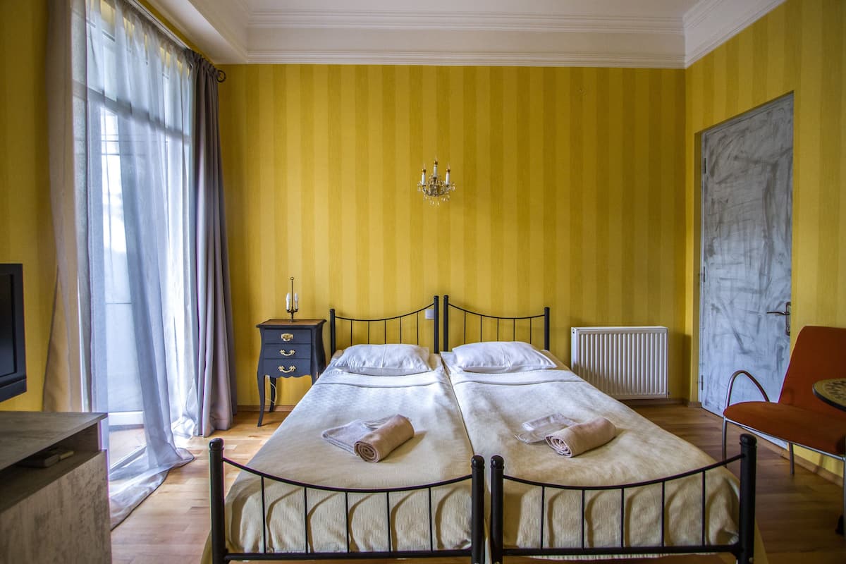 A room with two beds, a small table, a chair, a dresser, and a radiator.