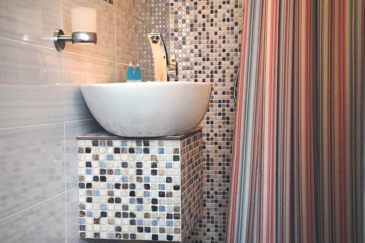 A bathroom with a white vessel sink, mosaic tile backsplash, and striped shower curtain.