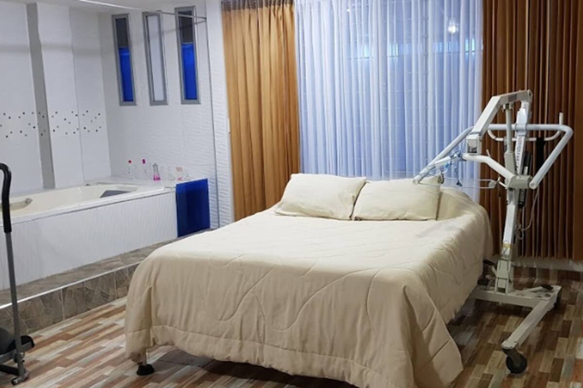 Una habitación de hospital con una cama, una cama clínica, un televisor y una ventana con cortinas.