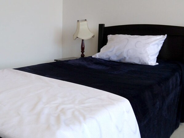 A neatly made bed with a white and dark blue bedspread, a white pillow, and a bedside lamp on a nightstand. - Hotel Siloe (Nobsa)