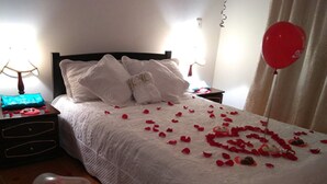 Una cama con pétalos de rosa y un arreglo de globos en forma de corazón.