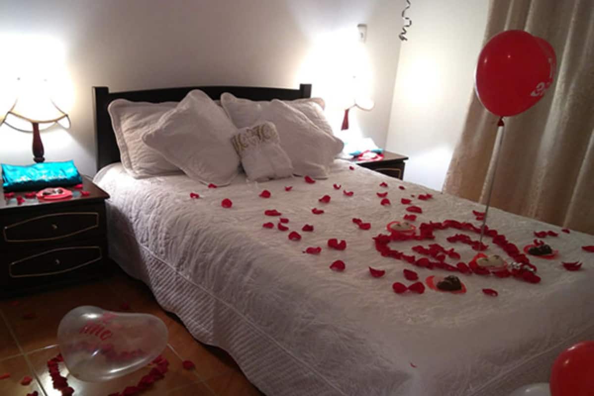 Una cama con pétalos de rosa y un arreglo de globos en forma de corazón.