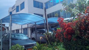 Un hotel moderno con estacionamiento techado, un coche y abundante vegetación.