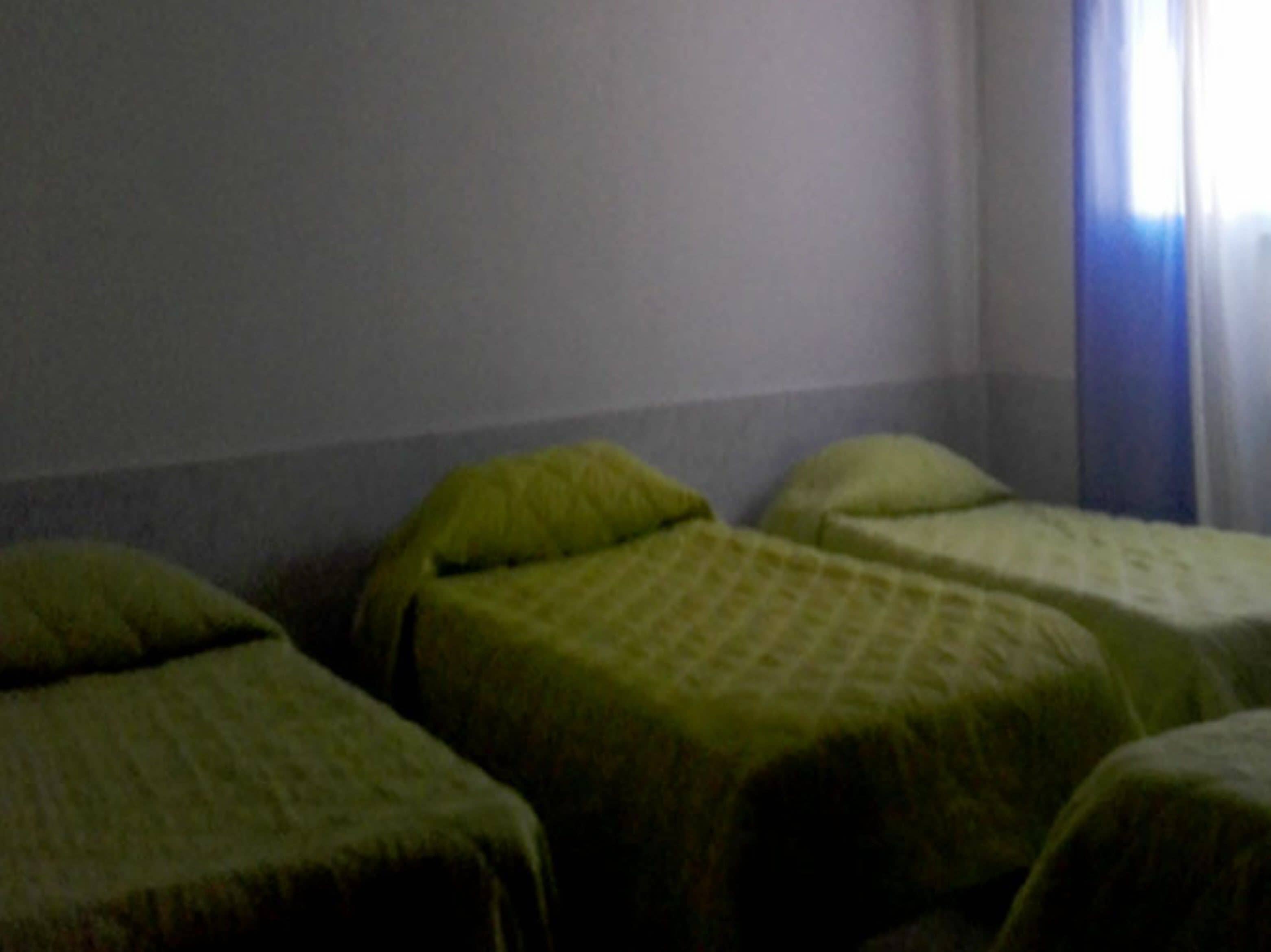 Una habitación con tres camas individuales, cada una con una colcha verde.