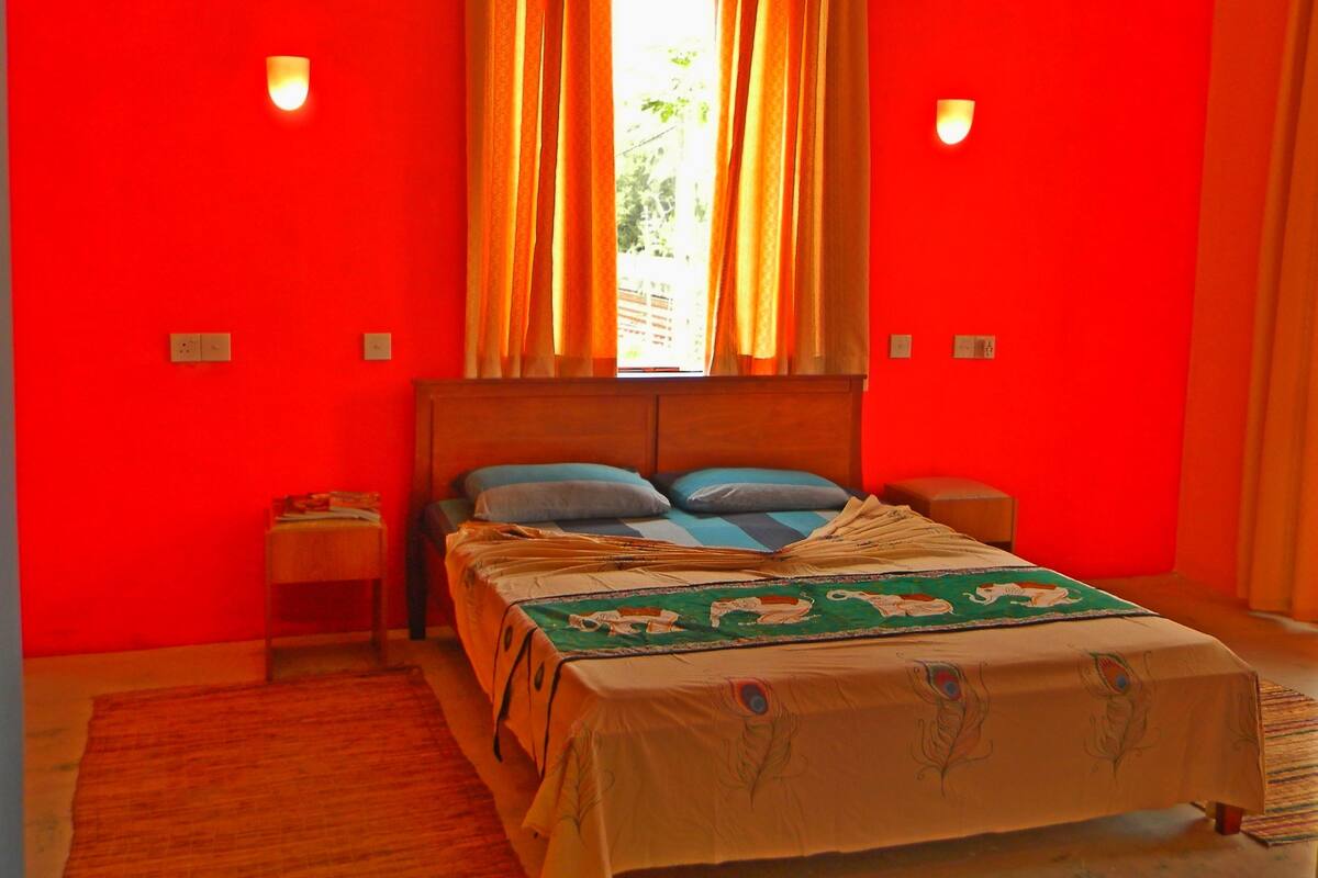 A room with a bed, two bedside tables, a window with curtains, and wall-mounted lights.