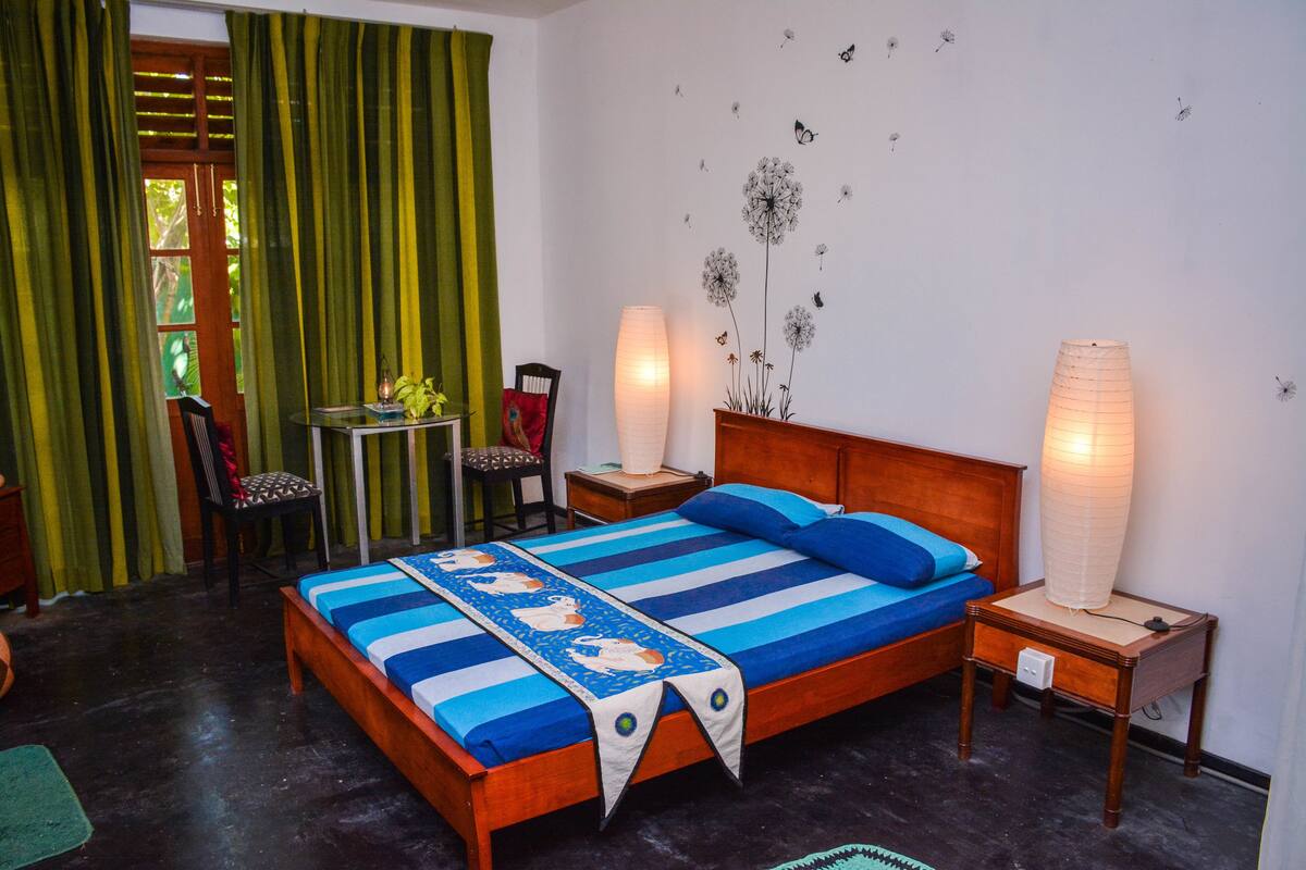 A bedroom with a bed, two bedside tables, a chair, a small table, and a window with curtains.