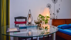 A glass table with a lamp, a plant, and a book. A red pillow and a blue sofa are in the background. - Raj Mahal Inn (Wadduwa)