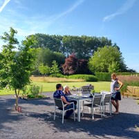 Un espacio al aire libre con mesa y sillas, rodeado de árboles y un seto.