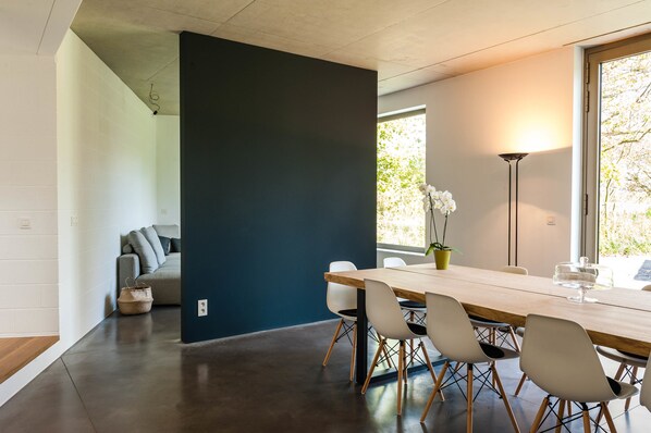 A modern dining area with a long wooden table, white chairs, and a dark accent wall.