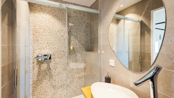 Een moderne badkamer met een douchewand met een steenachtige textuur, een ronde spiegel en een houten aanrechtblad.