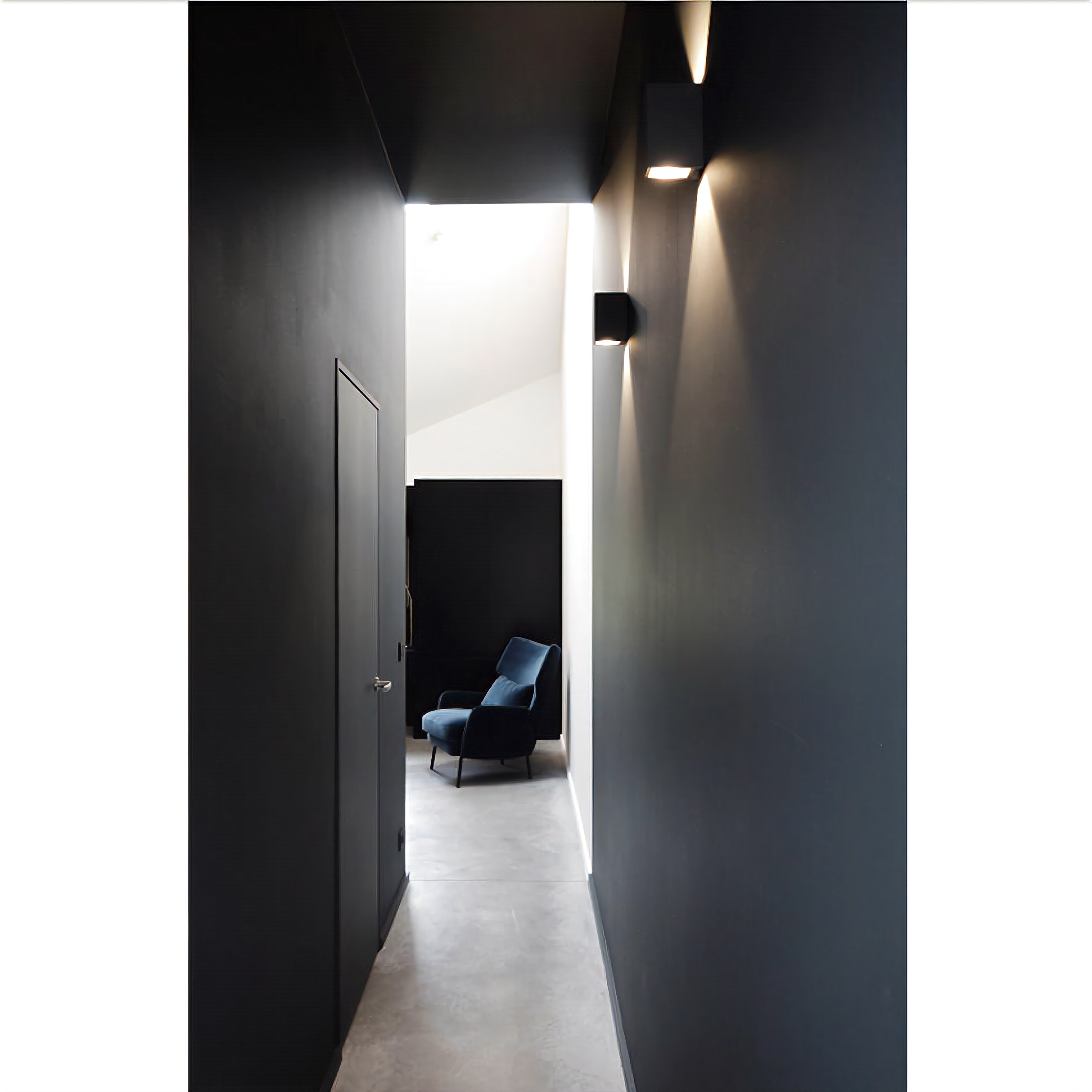 A narrow hallway with a door on the left and a blue chair in the center.