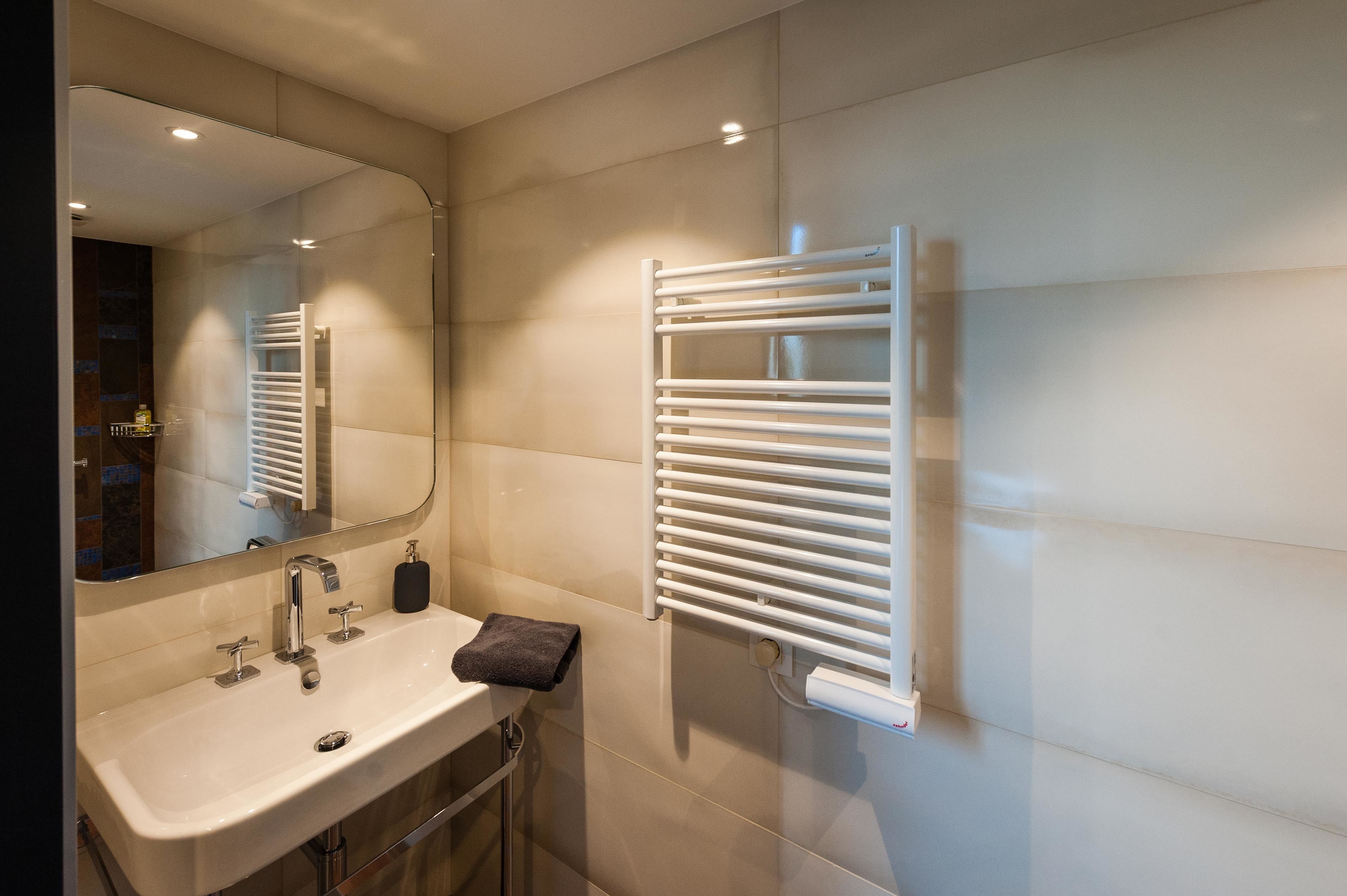 Une salle de bain moderne avec un lavabo blanc, un miroir et un porte-serviettes.