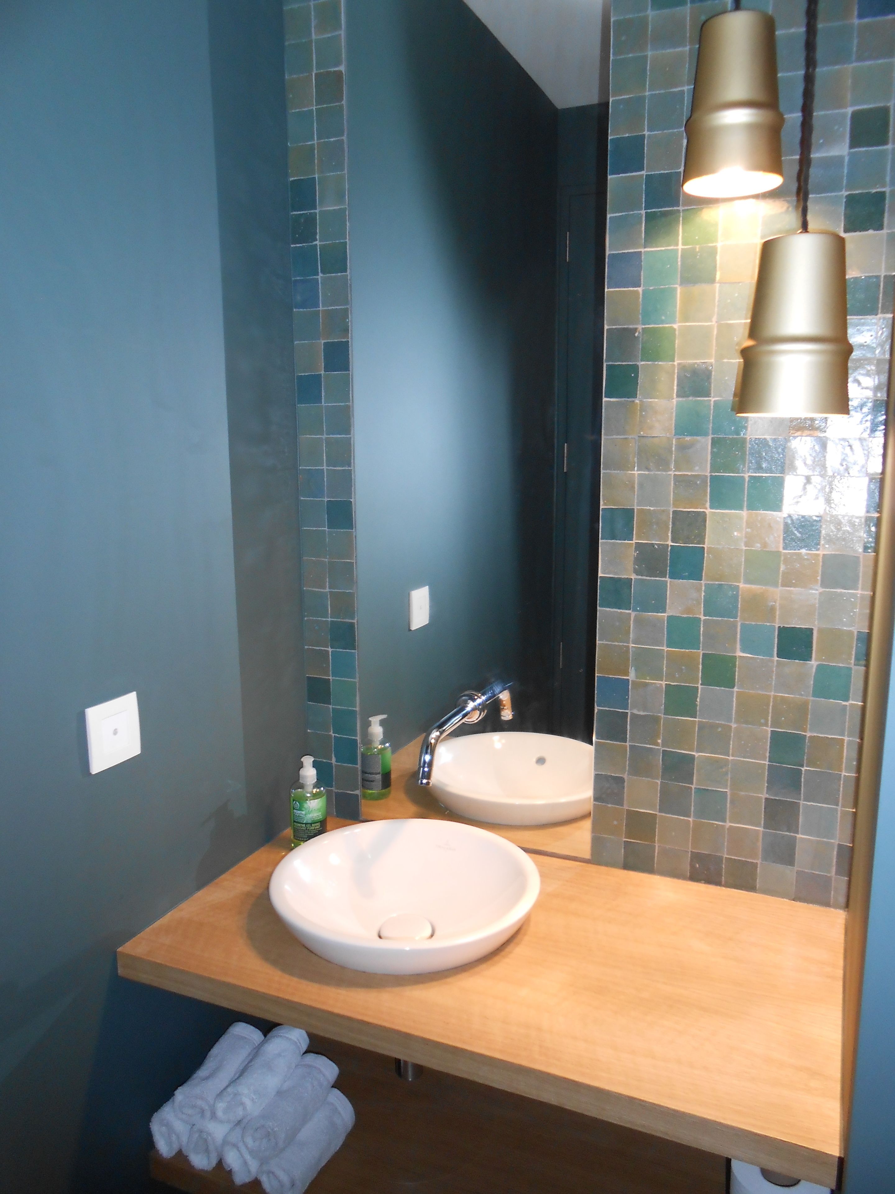 Une salle de bain avec un meuble-lavabo en bois, deux vasques et un miroir agrémenté d’un pare-feu en mosaïque.