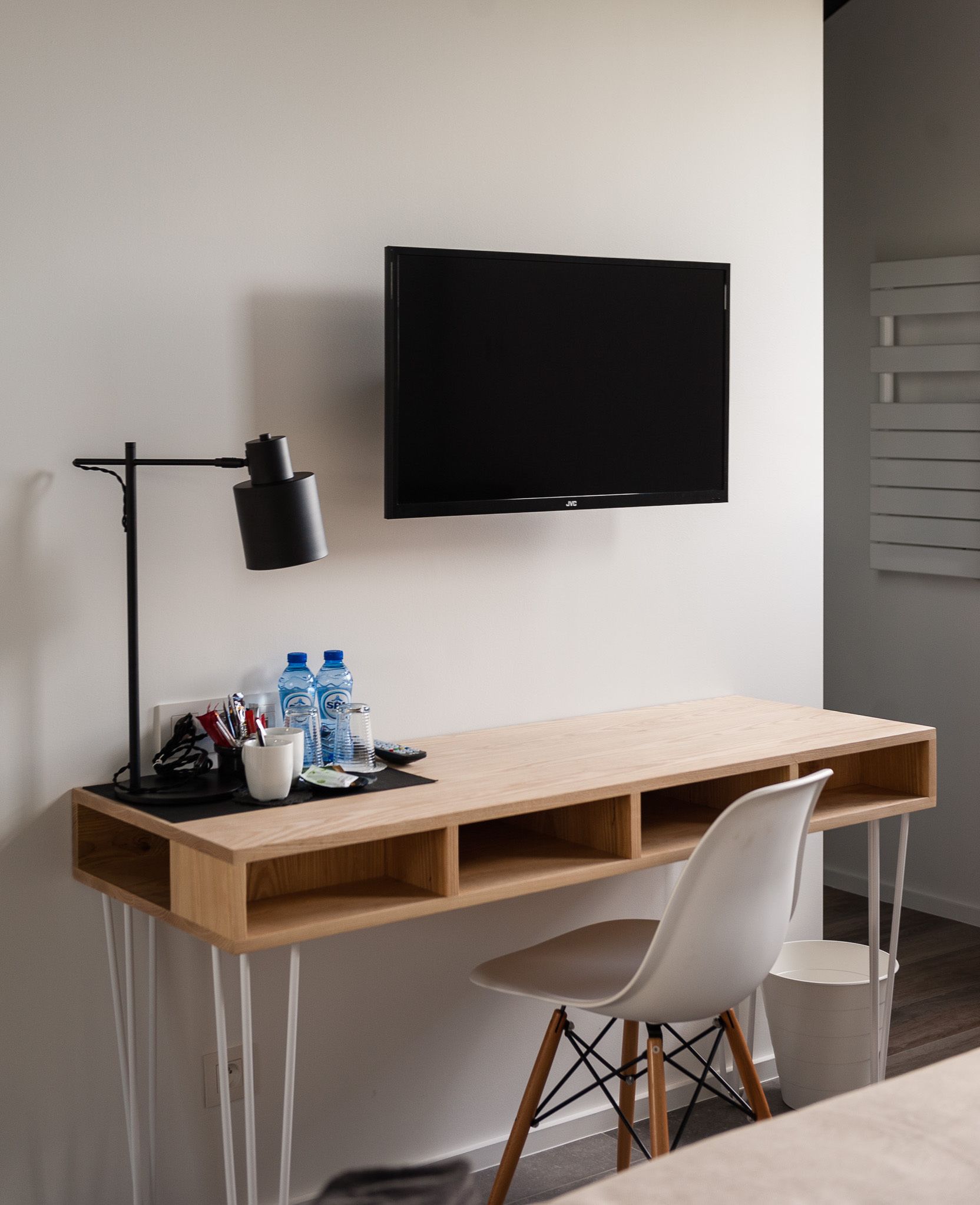 Een moderne werkruimte met een houten bureau, een witte stoel, een zwarte bureaulamp en een bevestigde televisie.