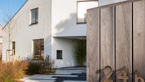 A modern building with a minimalist design, featuring a wooden fence with the number '24b' and a black and white pathway leading to the entrance. - Dimensions M (Mont-Saint-Guibert)