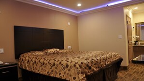 A hotel room with a large bed, a dark headboard, and a bathroom with a mirror and sink. - Sun Light Motel (Downey)