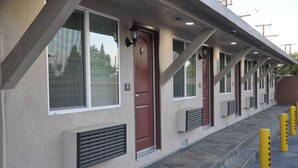 A row of hotel rooms with individual doors, windows, and air conditioning units. - Sun Light Motel (Downey)