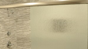 A shower with a glass door, a towel rack with a towel, and a tiled wall with a pattern. - Sun Light Motel (Downey)