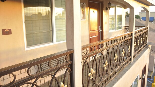 A hotel exterior with a balcony, a door, and a window with a number sign. - Sun Light Motel (Downey)