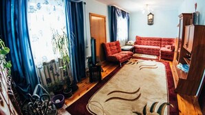 Un salon avec un canapé rouge, un plancher en bois, un tapis beige et des rideaux bleus.