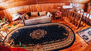 L’intérieur chaleureux d’un chalet avec un plafond en bois, un canapé, un tapis à motifs et une rambarde en bois.