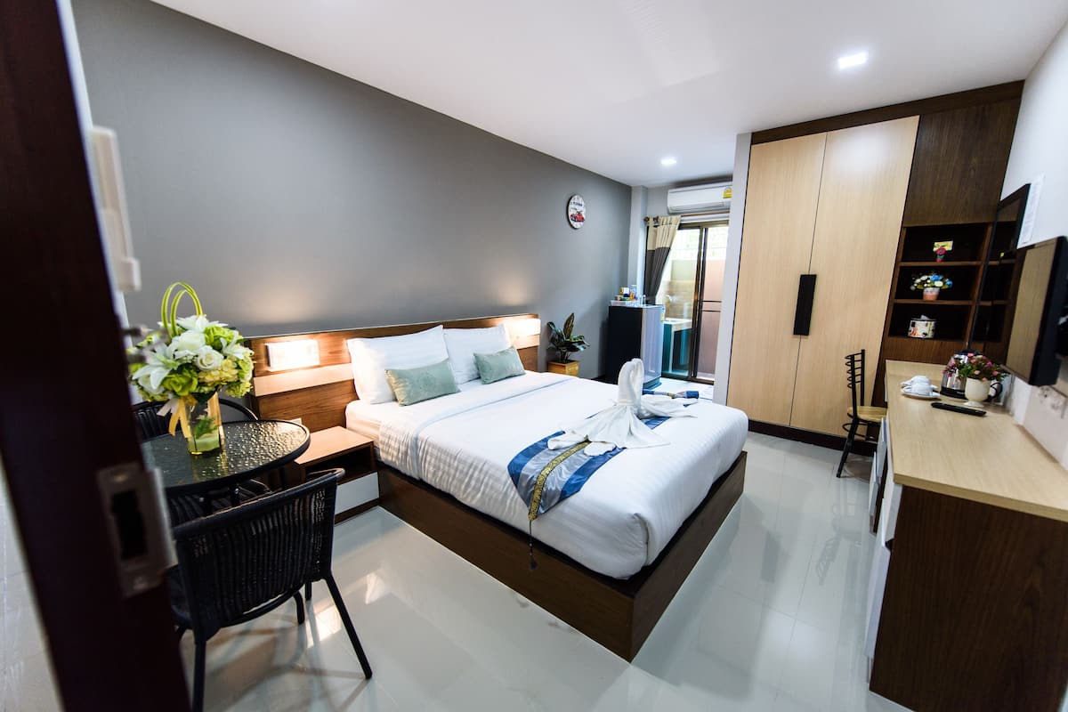 A modern hotel room with a neatly made bed, a small dining table, and a compact kitchenette.