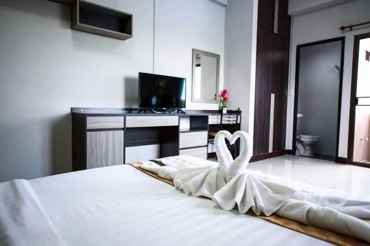 A hotel room with a bed, a desk with a television, a mirror, and a heart-shaped towel on the bed.