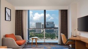 Une chambre d’hôtel équipée d’un lit, d’un bureau, d’une chaise, d’une petite table et d’une grande fenêtre donnant sur la ville.