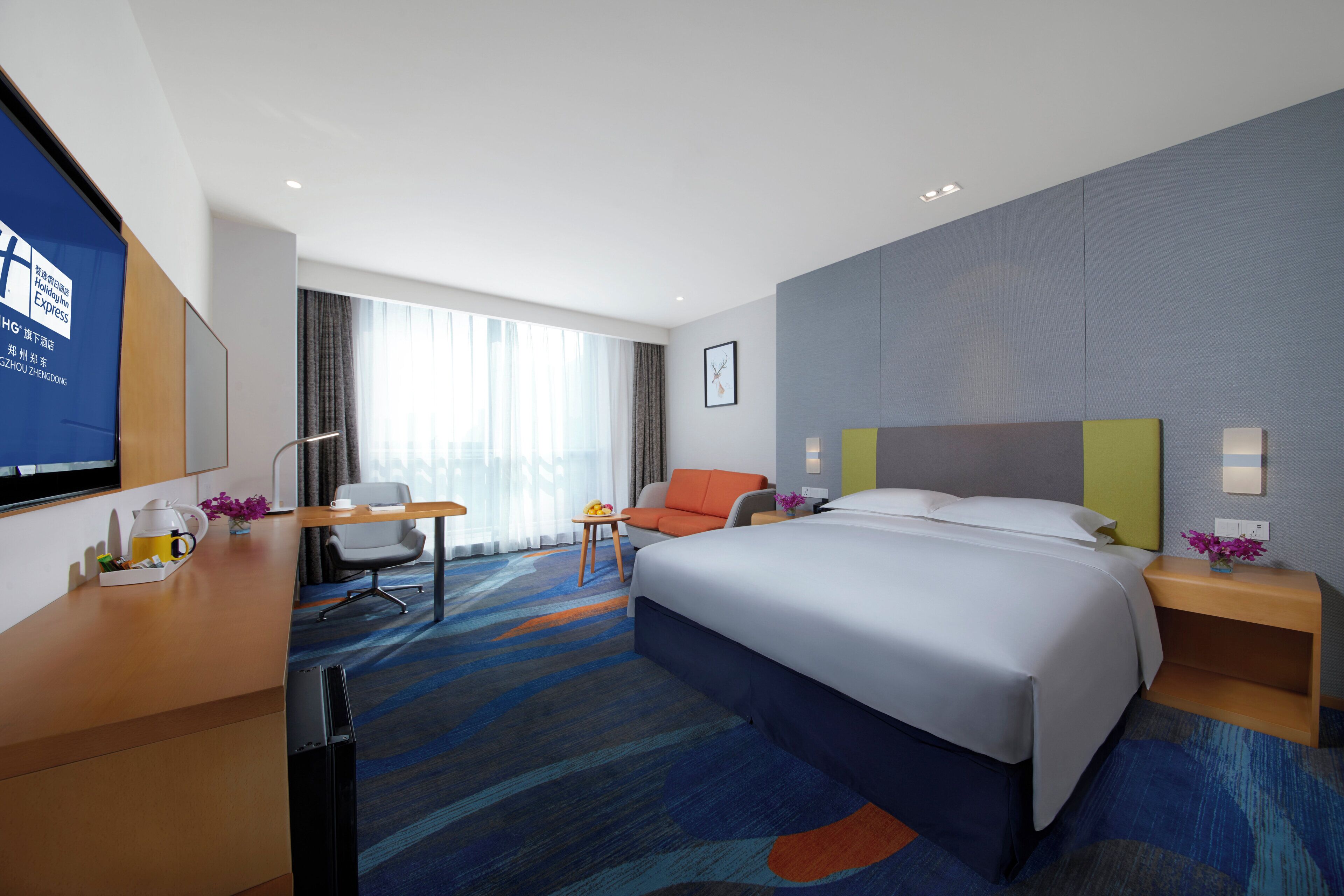 Une chambre d’hôtel avec un lit, un bureau, une chaise, une télévision et une fenêtre avec des rideaux.