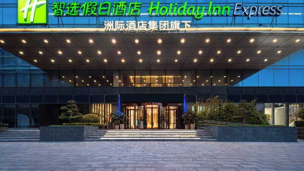 Un bâtiment de la chaîne Holiday Inn Express, doté d’une façade moderne, de grandes fenêtres en verre et d’une entrée bien éclairée.