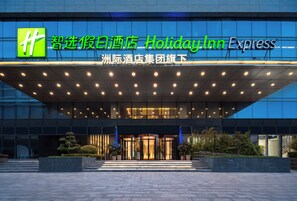 Un bâtiment de la chaîne Holiday Inn Express, doté d’une façade moderne, de grandes fenêtres en verre et d’une entrée bien éclairée.
