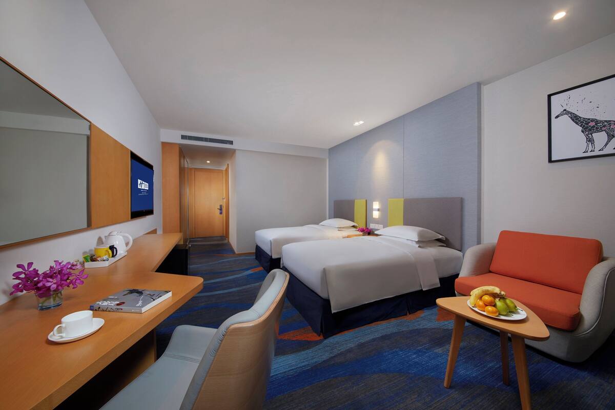 Ein Hotelzimmer mit einem Bett, zwei Nachttischen, einem Schreibtisch mit Stuhl, einem Sofa und einem kleinen Tisch mit Früchten.