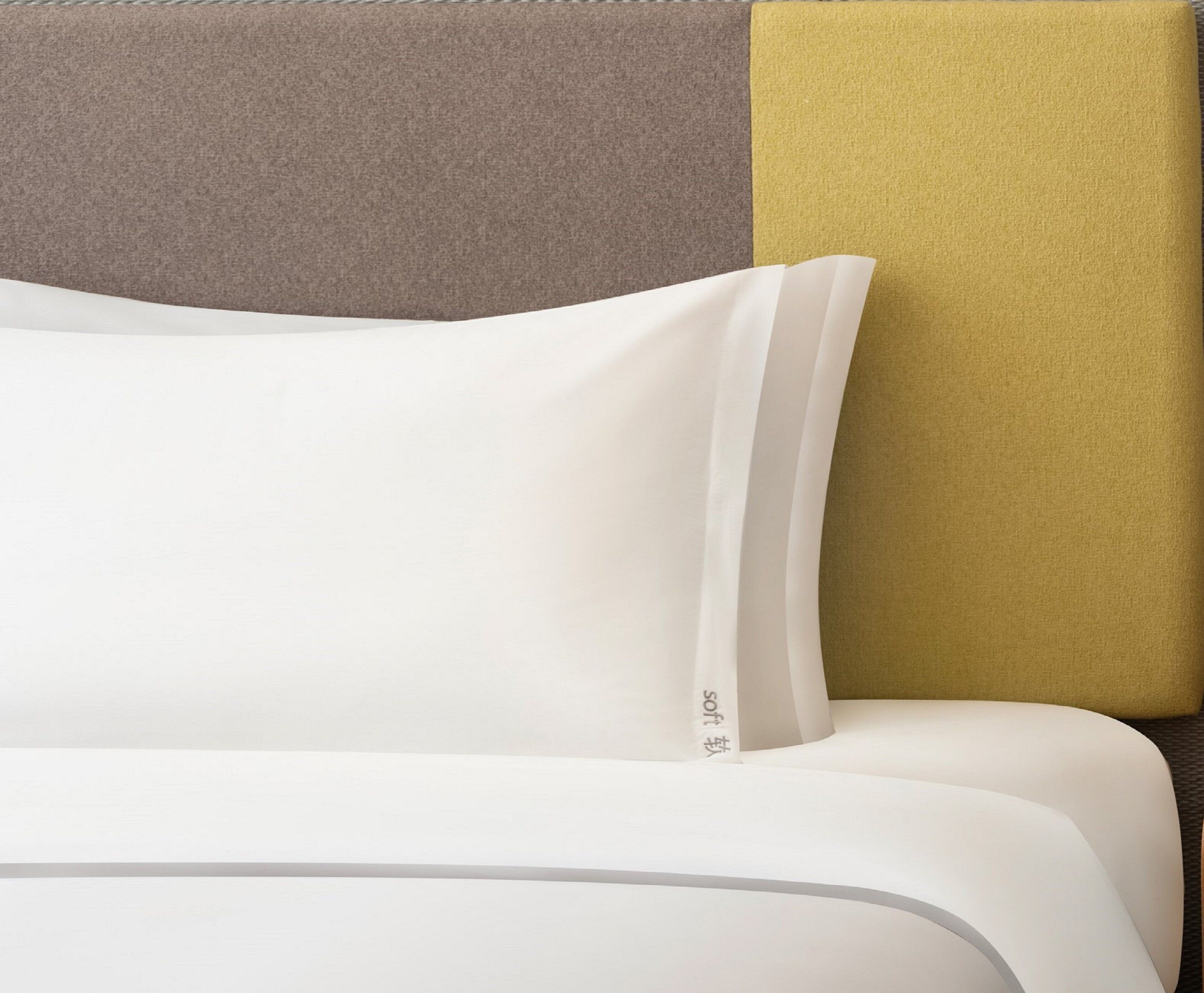 Ein Bett mit weißer Bettwäsche und einem Kopfkissen mit sichtbarem Markenlogo.