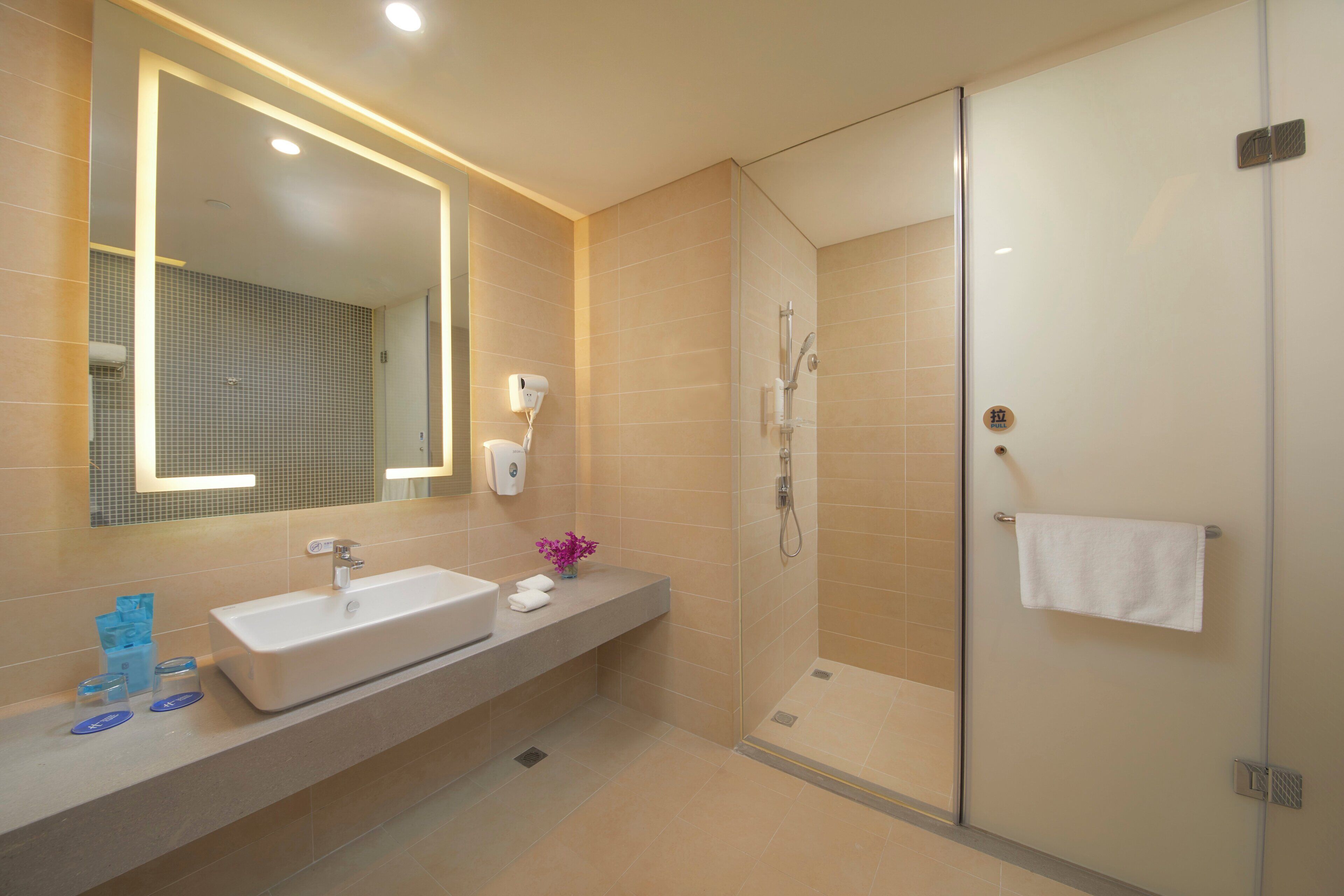 A modern bathroom with a large mirror, a sink, and a glass-enclosed shower area.